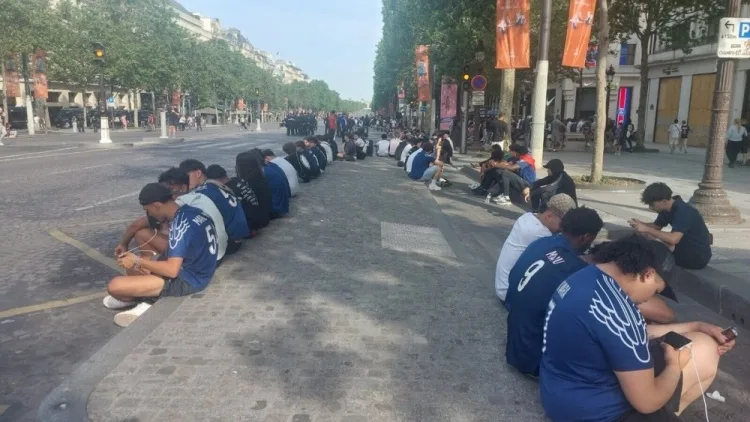 Ngồi xếp hàng dài, các cổ động viên quá cố Paris theo dõi trận đấu trên đại lộ Champs Elysées trên điện thoại di động
